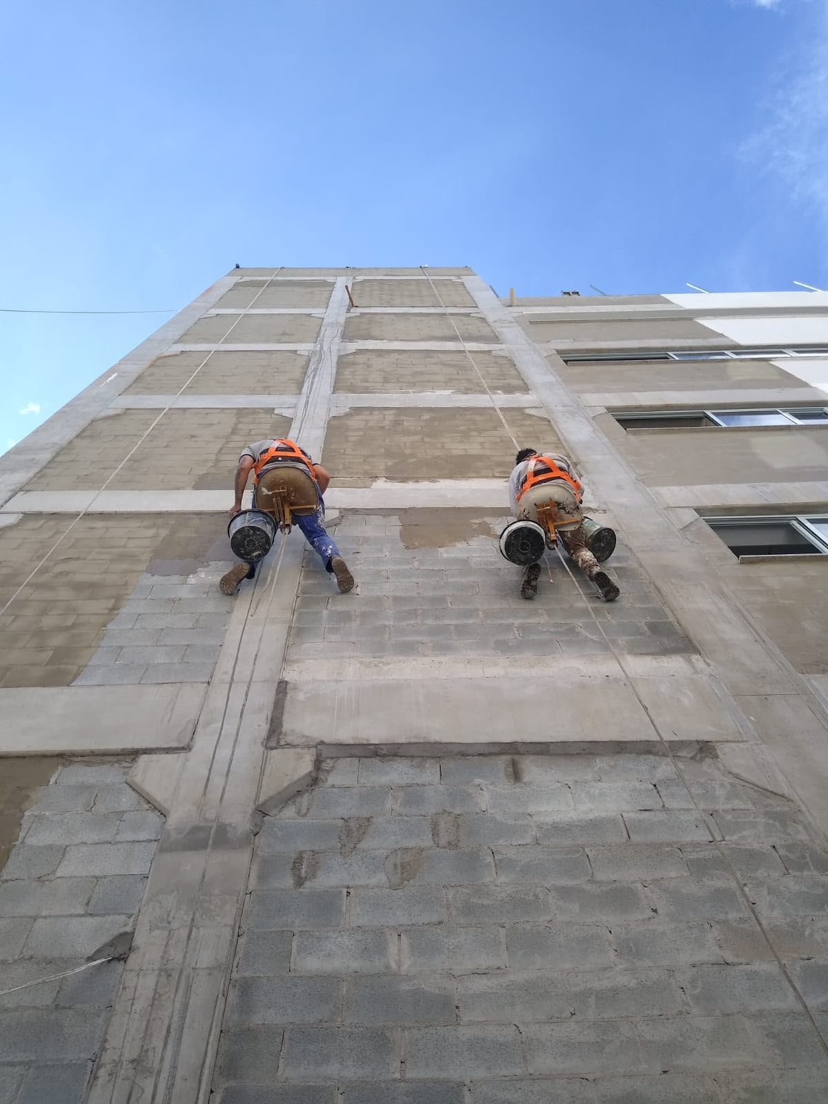 Profissionais em rapel pintando a fachada de um prédio alto