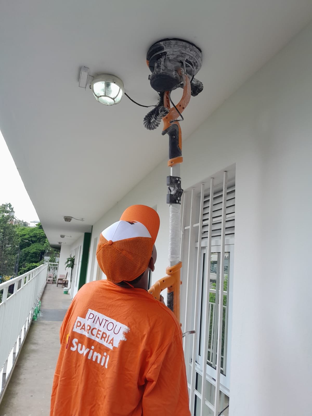 Profissional uniformizado lixando o teto com lixadeira de extensão