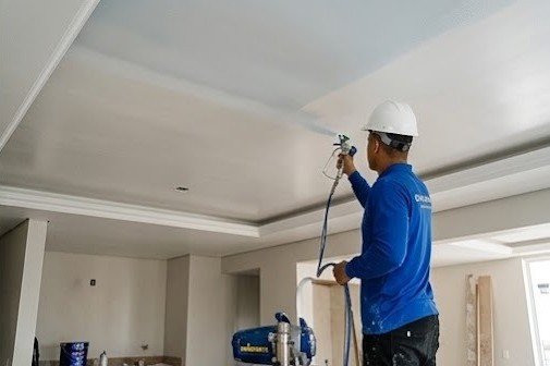Profissional pintando teto com pistola em ambiente amplo